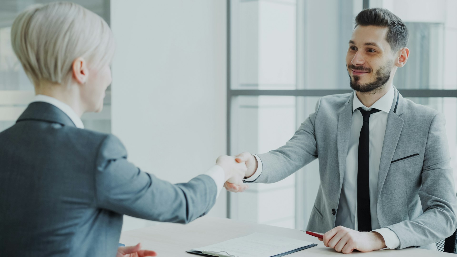 Two professionals shaking hands across a table after a successful interview